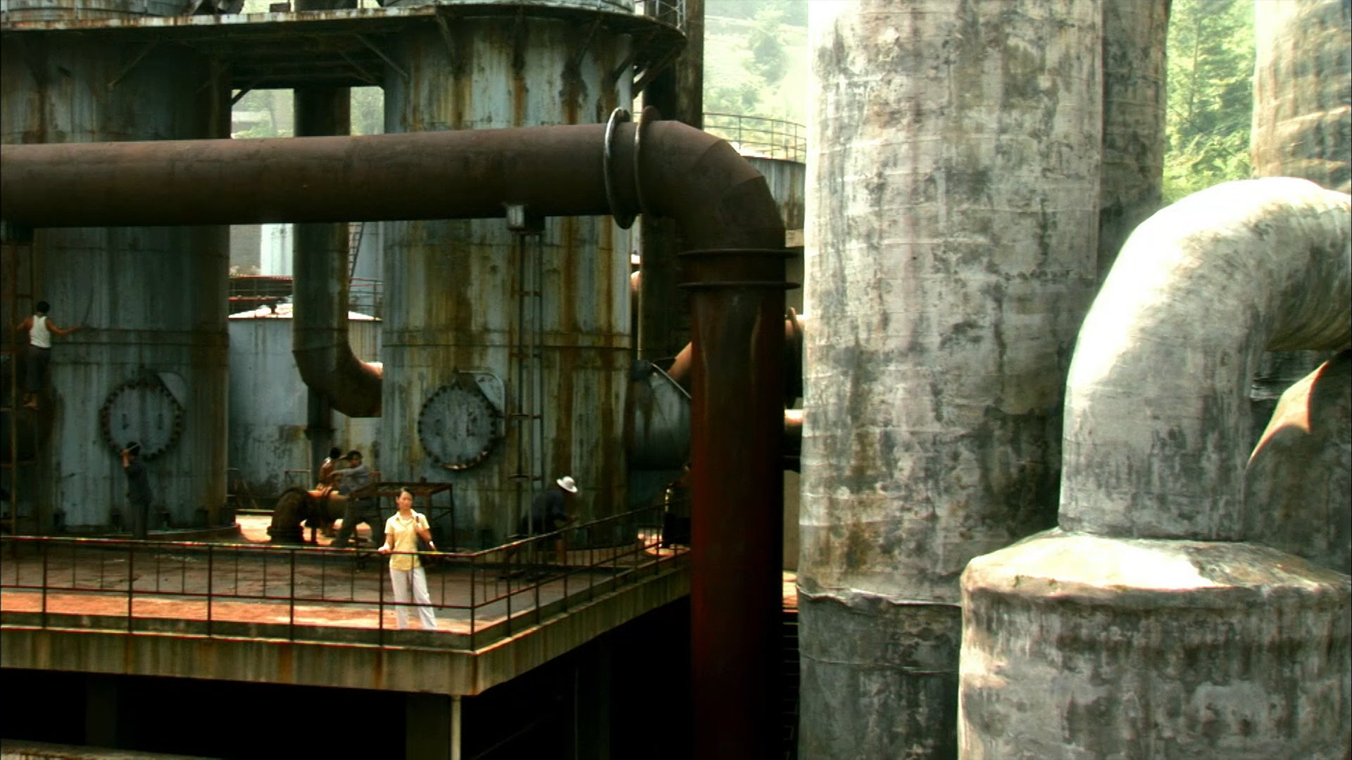 Long shot of woman standing next to big industrial pipes